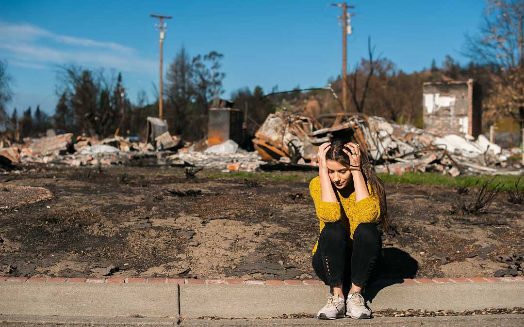 Woman sitting in front of her home after a natural disaster